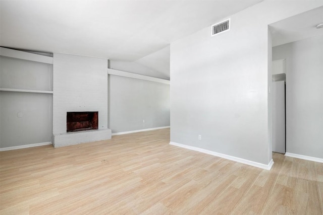 unfurnished living room with a brick fireplace, visible vents, baseboards, and wood finished floors