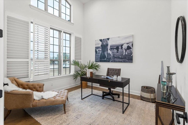 office featuring a towering ceiling, plenty of natural light, baseboards, and wood finished floors