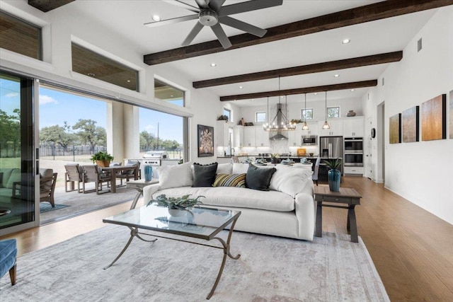 living room with a chandelier, beam ceiling, a towering ceiling, and light wood-style floors