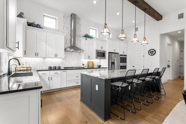 kitchen featuring visible vents, wall chimney exhaust hood, appliances with stainless steel finishes, white cabinetry, and a sink