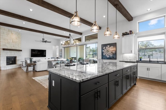 kitchen with a stone fireplace, hardwood / wood-style flooring, white cabinetry, and light stone countertops