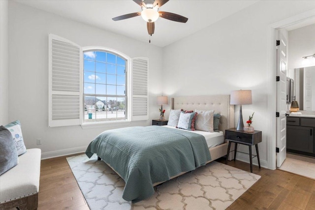 bedroom featuring ceiling fan, ensuite bath, wood finished floors, and baseboards