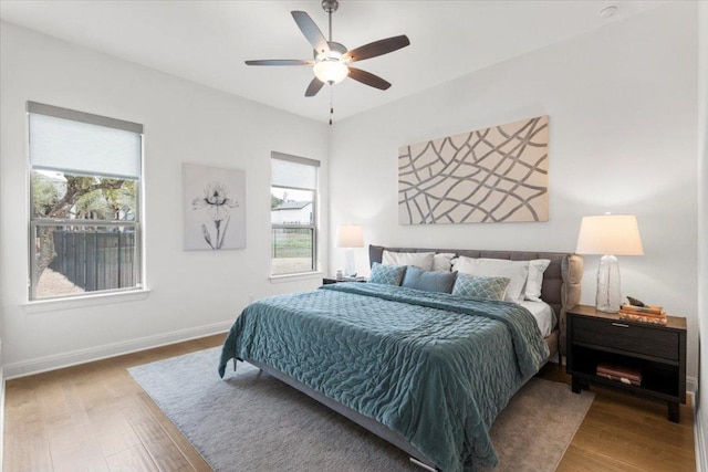 bedroom featuring ceiling fan, multiple windows, baseboards, and wood finished floors