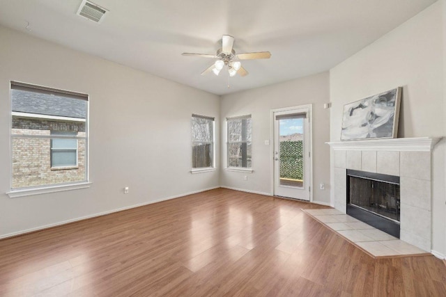 unfurnished living room with visible vents, a ceiling fan, wood finished floors, a tile fireplace, and baseboards