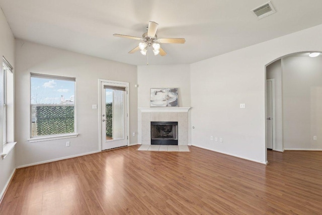 unfurnished living room featuring visible vents, arched walkways, wood finished floors, and a tile fireplace