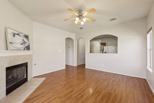 unfurnished living room featuring ceiling fan, wood finished floors, a tile fireplace, and visible vents