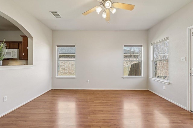 spare room featuring arched walkways, visible vents, ceiling fan, wood finished floors, and baseboards