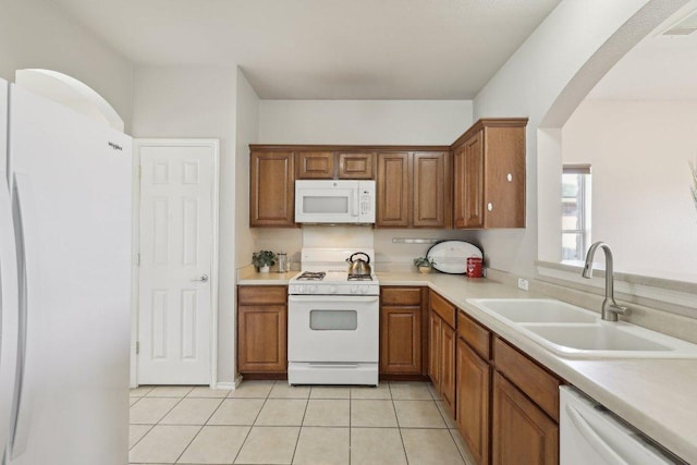 kitchen with white appliances, brown cabinetry, light tile patterned flooring, and a sink