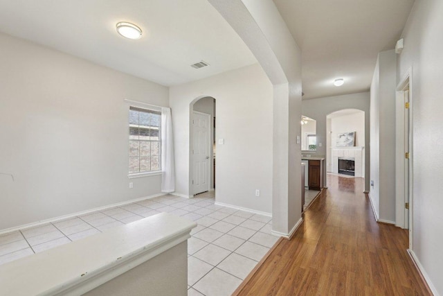 corridor with arched walkways, light tile patterned flooring, visible vents, and baseboards