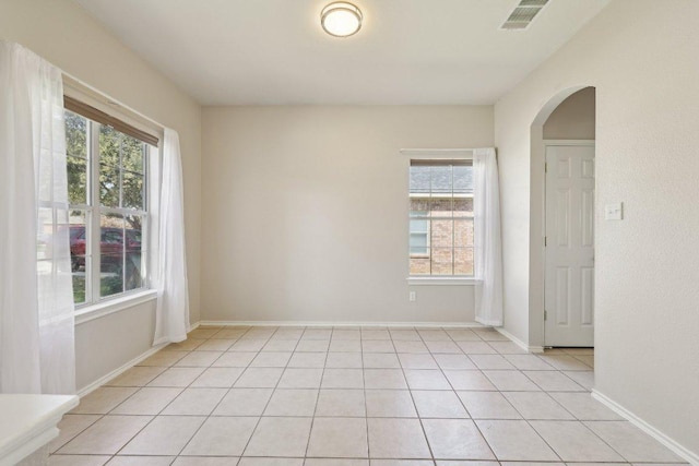 unfurnished room with arched walkways, light tile patterned floors, visible vents, and baseboards