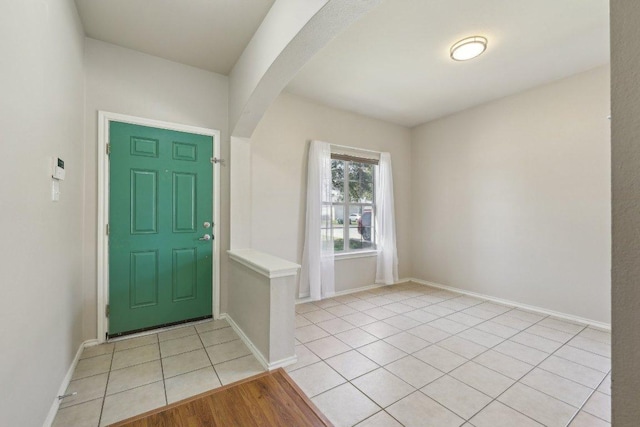 foyer featuring light tile patterned floors, baseboards, and arched walkways