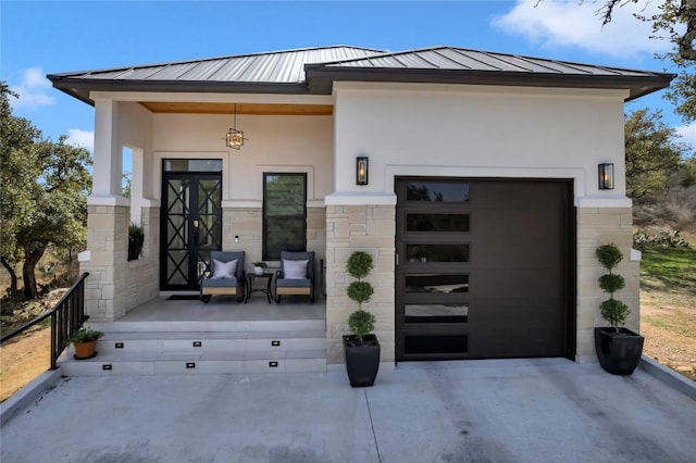 doorway to property featuring metal roof, an attached garage, concrete driveway, stucco siding, and a standing seam roof