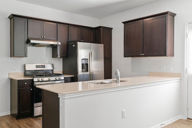 kitchen featuring appliances with stainless steel finishes, a sink, dark brown cabinetry, wood finished floors, and under cabinet range hood