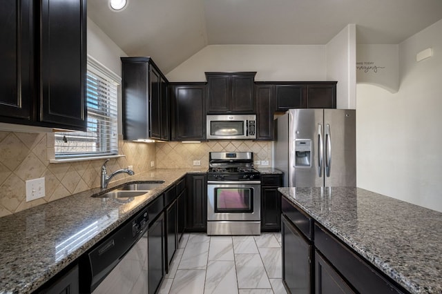 kitchen with tasteful backsplash, dark stone counters, appliances with stainless steel finishes, vaulted ceiling, and a sink