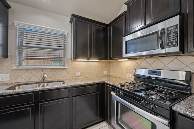 kitchen with appliances with stainless steel finishes, tasteful backsplash, a sink, and light stone countertops