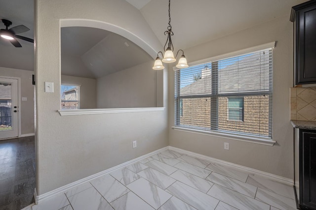 unfurnished dining area featuring marble finish floor, baseboards, vaulted ceiling, and ceiling fan with notable chandelier