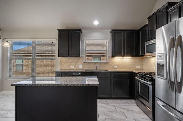 kitchen with stainless steel appliances, a kitchen island, marble finish floor, dark cabinetry, and dark stone counters