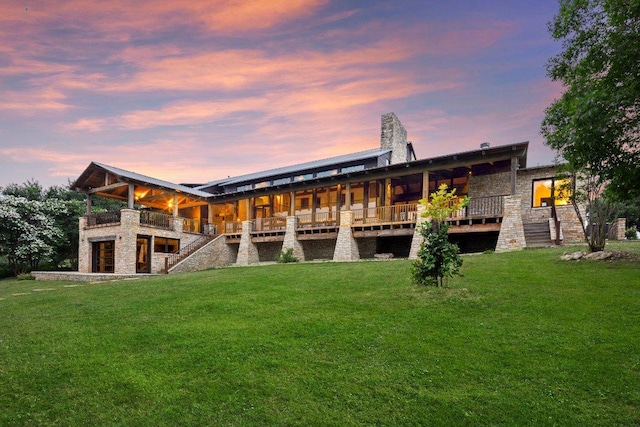 back of property at dusk with stairs, stone siding, a yard, and a chimney