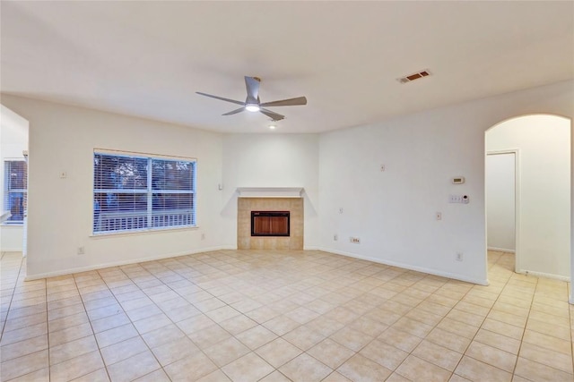 unfurnished living room featuring arched walkways, a fireplace, visible vents, a ceiling fan, and baseboards