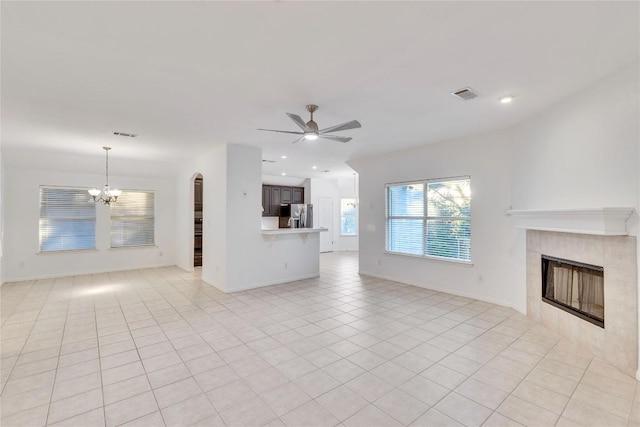 unfurnished living room featuring light tile patterned floors, visible vents, a tile fireplace, ceiling fan with notable chandelier, and recessed lighting