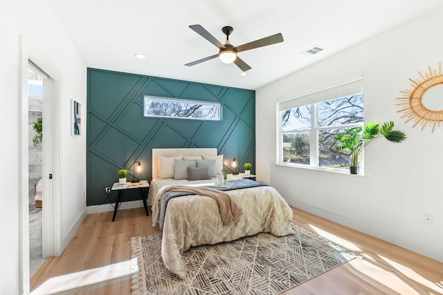 bedroom with light wood-style floors, baseboards, an accent wall, and visible vents