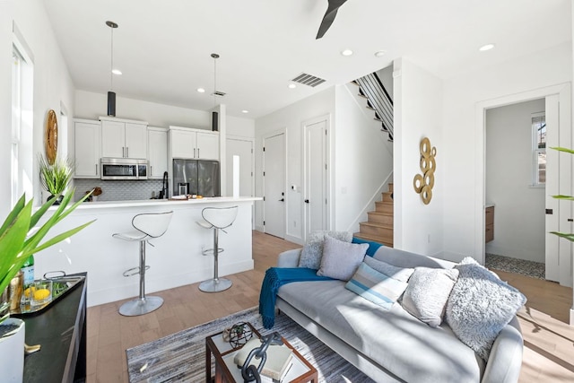 living area featuring stairs, light wood finished floors, visible vents, and recessed lighting