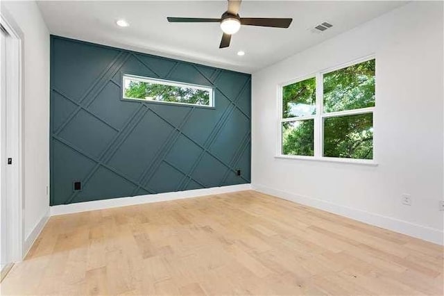 spare room with light wood-type flooring, plenty of natural light, an accent wall, and visible vents