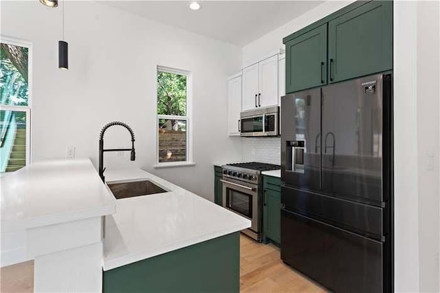 kitchen featuring a peninsula, appliances with stainless steel finishes, green cabinets, and a sink