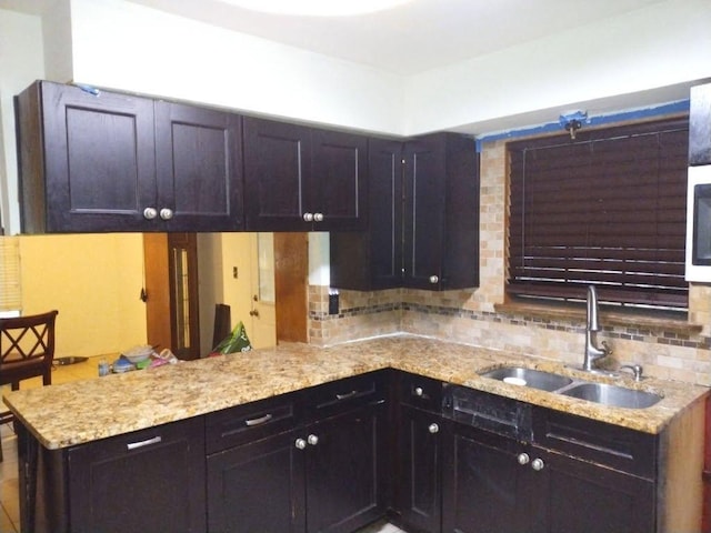 kitchen with a sink, backsplash, a peninsula, and light stone countertops