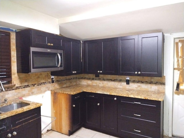 kitchen featuring light stone counters, light tile patterned floors, tasteful backsplash, stainless steel microwave, and a sink