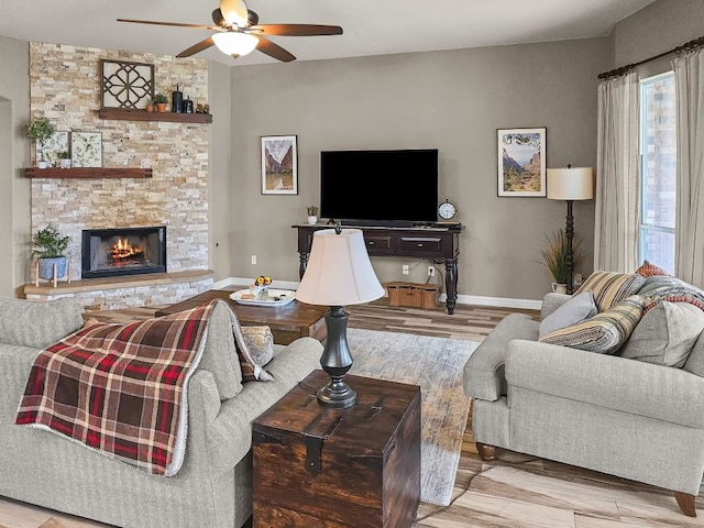 living area featuring ceiling fan, a fireplace, baseboards, and wood finished floors