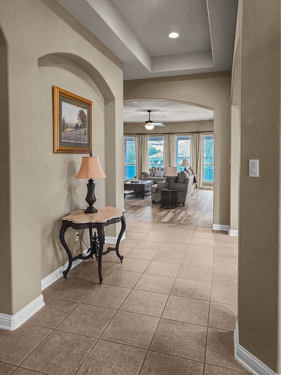 hall featuring baseboards, a tray ceiling, and tile patterned floors