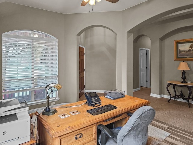 tiled home office with a ceiling fan, arched walkways, and baseboards