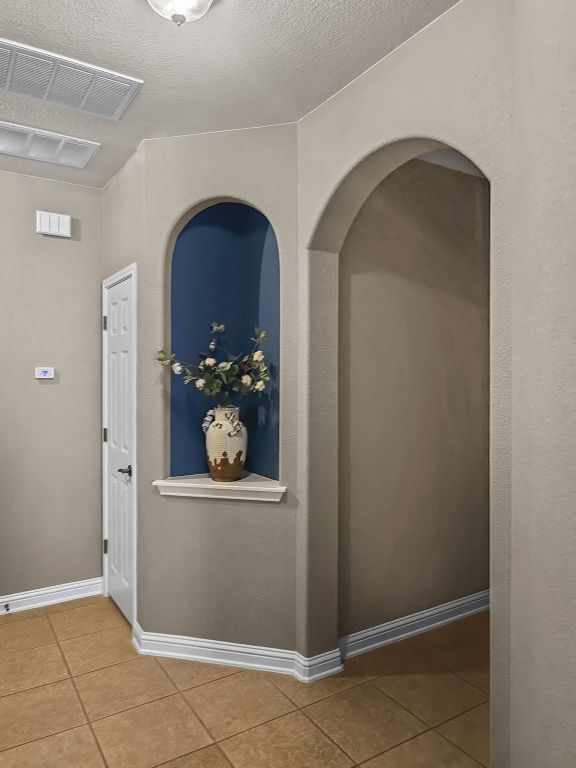 hall featuring light tile patterned floors, baseboards, visible vents, and a textured ceiling