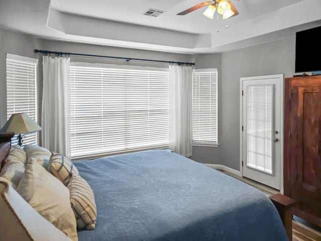 bedroom with a raised ceiling, visible vents, ceiling fan, and baseboards