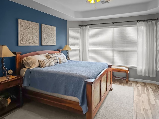 bedroom featuring ceiling fan, visible vents, baseboards, light wood-type flooring, and a raised ceiling