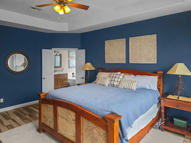 bedroom featuring ensuite bathroom, wood finished floors, a ceiling fan, visible vents, and baseboards