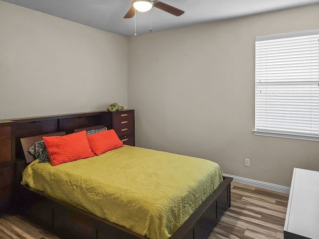 bedroom featuring a ceiling fan, multiple windows, baseboards, and wood finished floors