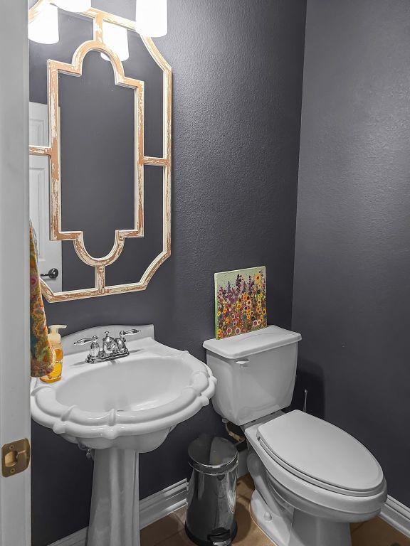 half bath with baseboards, a textured wall, and toilet