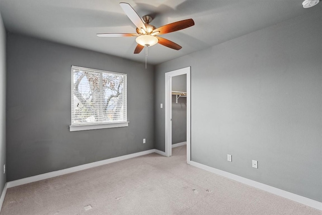 unfurnished bedroom with a walk in closet, a closet, a ceiling fan, carpet flooring, and baseboards