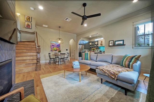 living area featuring wood finished floors, visible vents, a ceiling fan, stairway, and crown molding