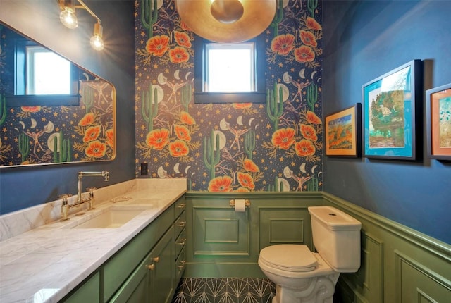 bathroom featuring wainscoting, a decorative wall, vanity, and toilet