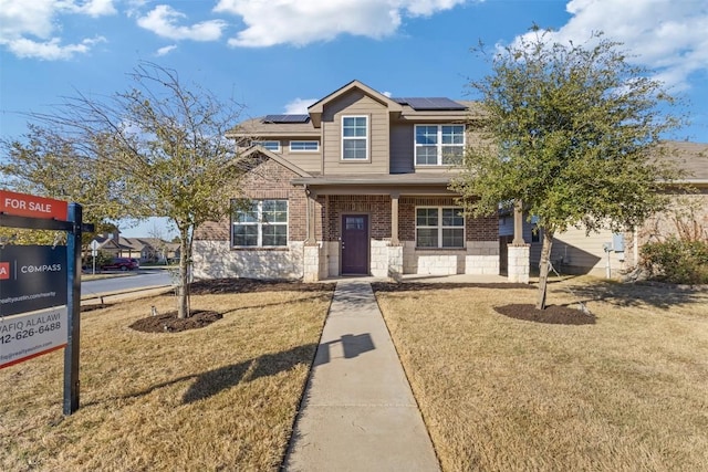 craftsman-style home with covered porch, solar panels, brick siding, and a front yard