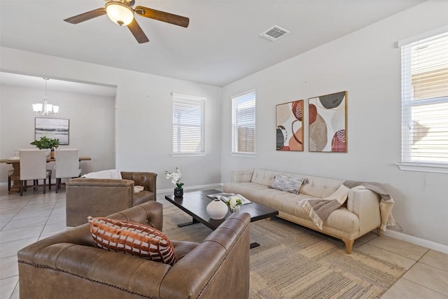 living room featuring light tile patterned floors, baseboards, visible vents, and ceiling fan with notable chandelier