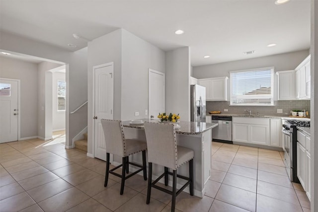 kitchen featuring light stone counters, stainless steel appliances, visible vents, a kitchen breakfast bar, and decorative backsplash