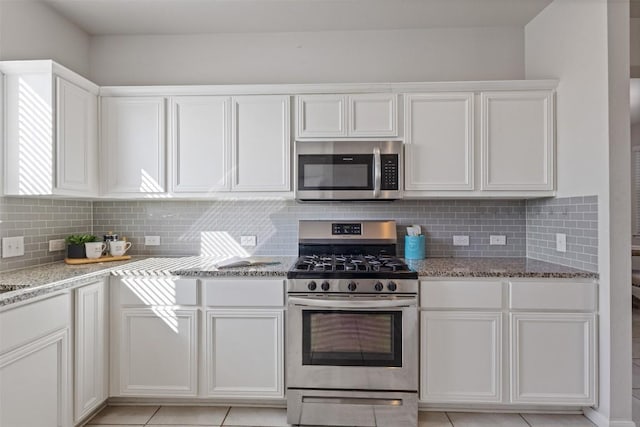 kitchen featuring light stone countertops, appliances with stainless steel finishes, white cabinets, and decorative backsplash