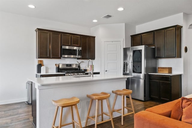 kitchen with a sink, visible vents, appliances with stainless steel finishes, backsplash, and dark wood-style floors