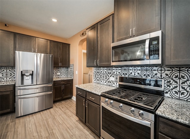 kitchen with arched walkways, light stone counters, dark brown cabinets, appliances with stainless steel finishes, and tasteful backsplash