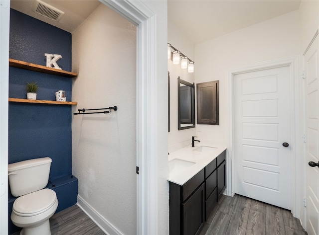 bathroom with double vanity, visible vents, toilet, a sink, and wood finished floors