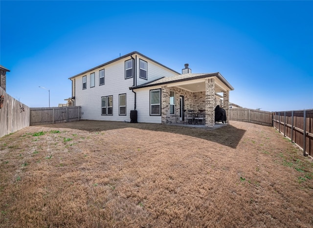 back of house featuring a fenced backyard, a patio, a chimney, and a lawn